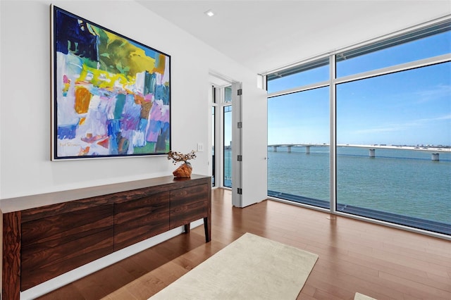 interior space with expansive windows, a water view, and hardwood / wood-style flooring