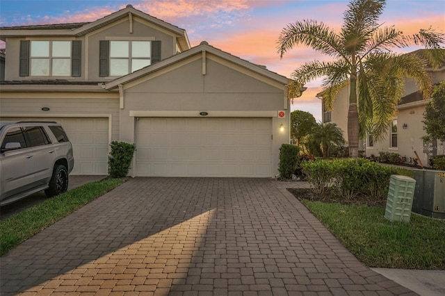 traditional-style house featuring a garage, decorative driveway, and stucco siding