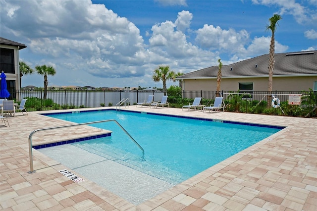 community pool with a patio area, fence, and a water view