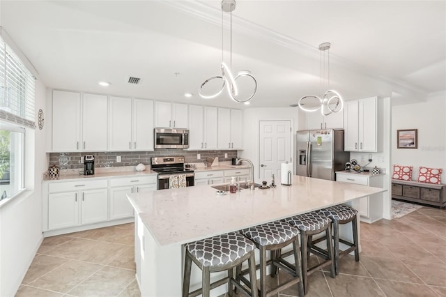 kitchen featuring appliances with stainless steel finishes, sink, white cabinets, hanging light fixtures, and an island with sink