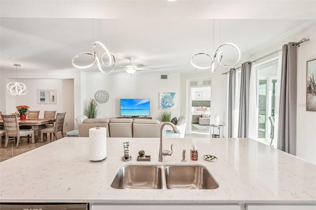 kitchen with light stone counters, decorative light fixtures, visible vents, a sink, and an island with sink