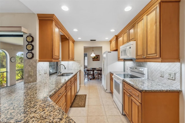 kitchen with sink, white appliances, hanging light fixtures, and stone countertops