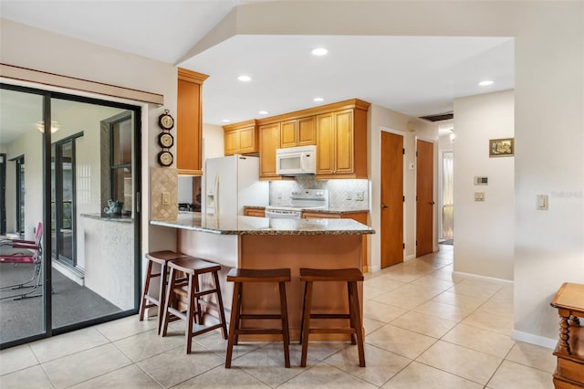 kitchen with stone countertops, backsplash, white appliances, and a breakfast bar area