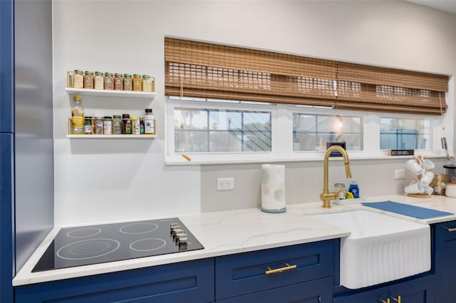 kitchen with black electric stovetop, light stone counters, blue cabinets, and sink