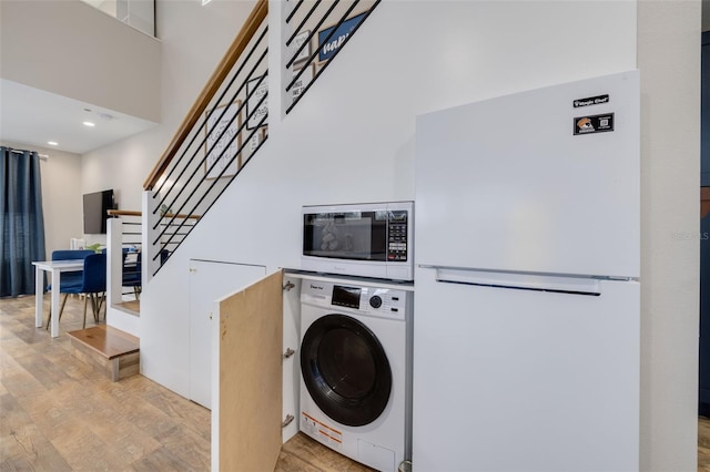 clothes washing area featuring washer / dryer, a towering ceiling, and light hardwood / wood-style floors