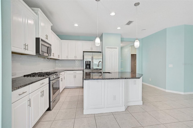 kitchen featuring dark stone countertops, white cabinetry, an island with sink, and appliances with stainless steel finishes