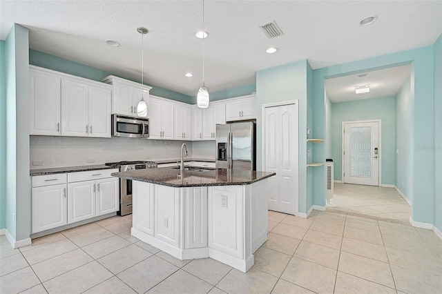 kitchen featuring dark stone counters, white cabinetry, an island with sink, and stainless steel appliances