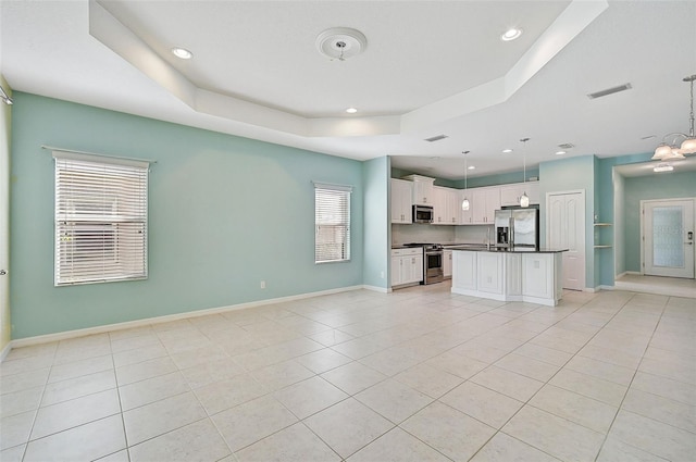 kitchen featuring appliances with stainless steel finishes, a raised ceiling, a kitchen island, decorative light fixtures, and white cabinetry