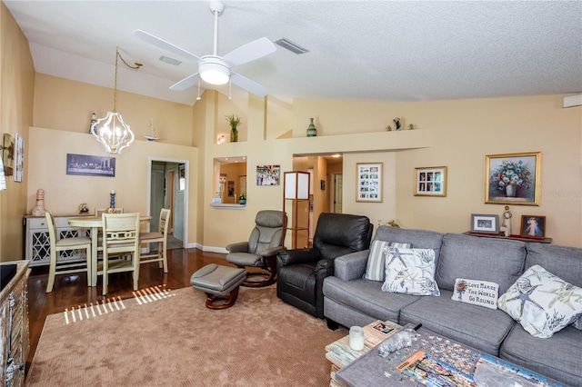 living area with visible vents, dark wood-style floors, a textured ceiling, high vaulted ceiling, and ceiling fan with notable chandelier