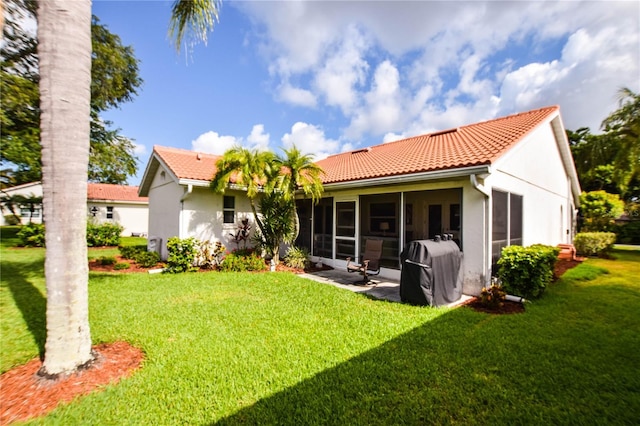 rear view of house featuring a sunroom, a lawn, a tiled roof, and stucco siding