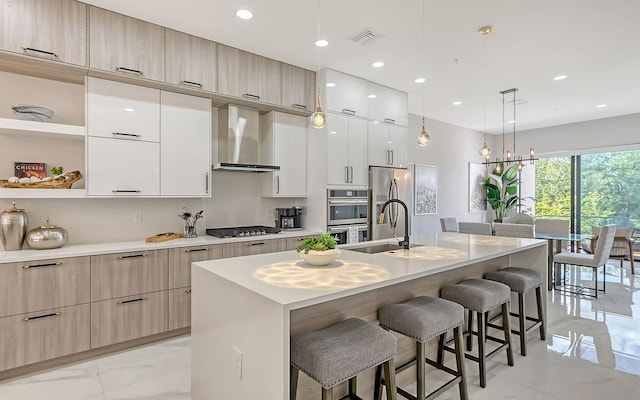 kitchen with a center island with sink, a kitchen breakfast bar, and wall chimney range hood