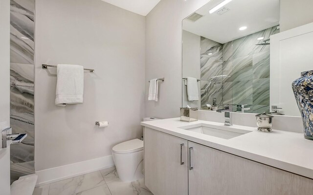 bathroom with a tile shower, vanity, and toilet
