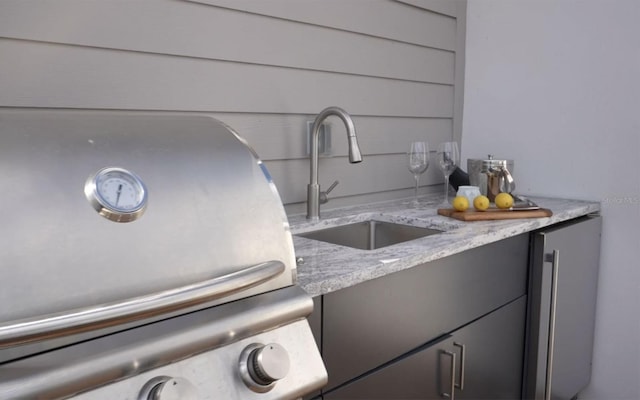 exterior details with light stone countertops, stainless steel fridge, and sink