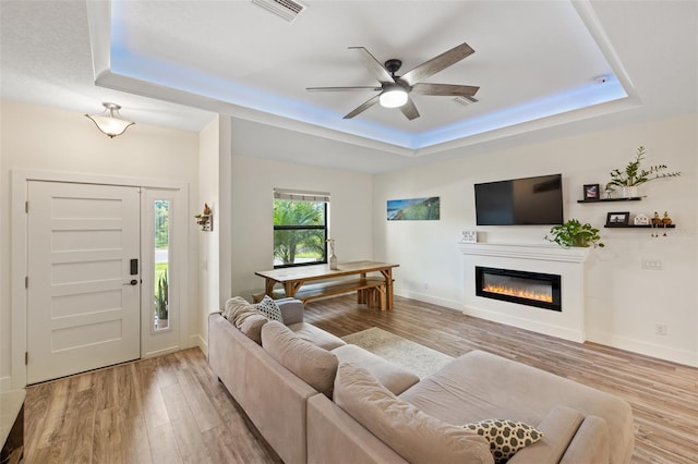 living room with a tray ceiling, light hardwood / wood-style flooring, and ceiling fan