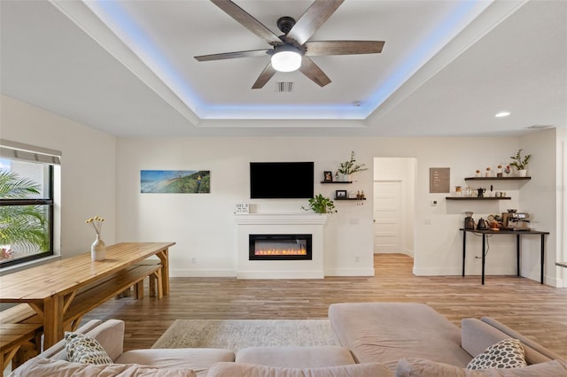 living room with ceiling fan, light hardwood / wood-style floors, and a tray ceiling