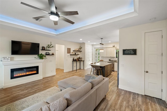 living room with light hardwood / wood-style flooring, a raised ceiling, and ceiling fan