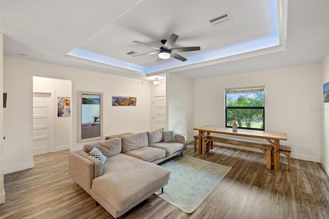 living room with ceiling fan, a raised ceiling, and light hardwood / wood-style flooring