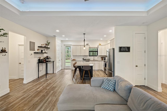 living room featuring light hardwood / wood-style floors, a raised ceiling, and sink