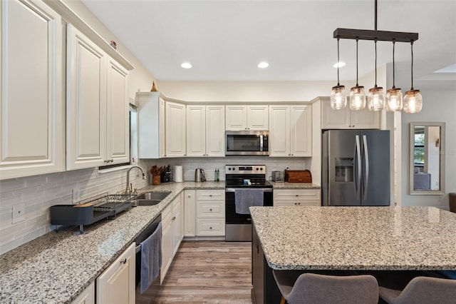 kitchen with a kitchen bar, sink, light hardwood / wood-style floors, light stone counters, and stainless steel appliances