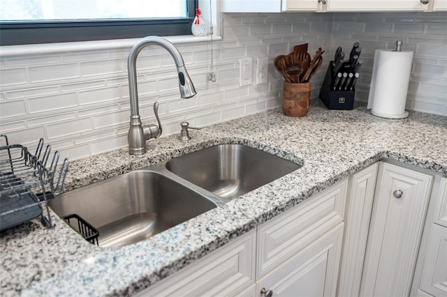 interior details with white cabinets, tasteful backsplash, light stone countertops, and sink