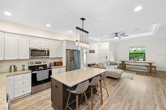 kitchen featuring a breakfast bar area, light stone counters, white cabinets, and appliances with stainless steel finishes