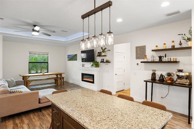 kitchen featuring light wood-type flooring, decorative light fixtures, light stone counters, and ceiling fan