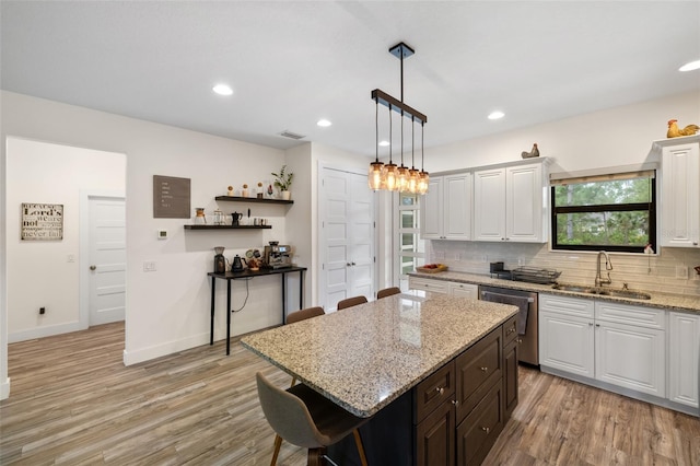 kitchen featuring dishwasher, white cabinets, sink, light hardwood / wood-style flooring, and a breakfast bar area