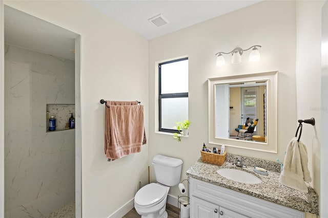 bathroom with tiled shower, vanity, toilet, and a healthy amount of sunlight