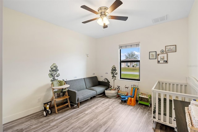 bedroom featuring a crib, light hardwood / wood-style floors, and ceiling fan