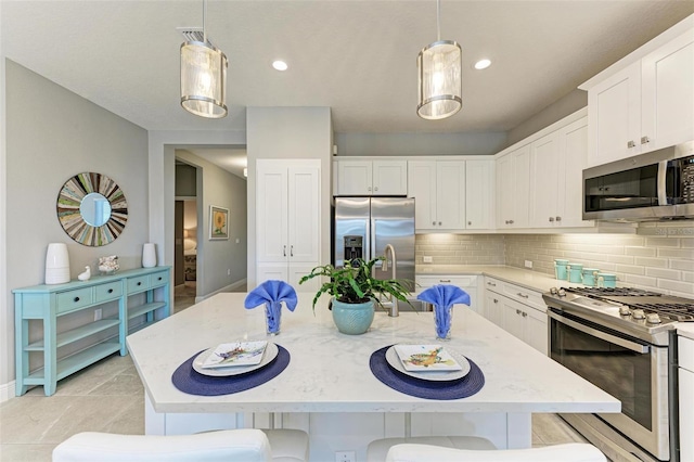 kitchen with appliances with stainless steel finishes, a breakfast bar area, a center island with sink, and decorative light fixtures