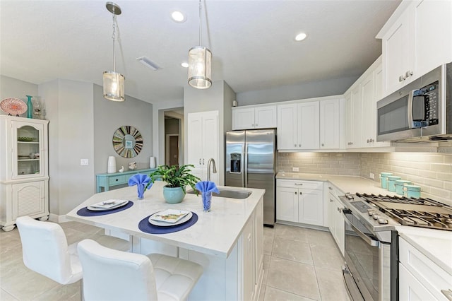 kitchen with sink, a kitchen island with sink, hanging light fixtures, stainless steel appliances, and white cabinets