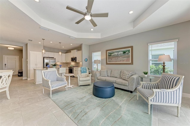 tiled living room featuring ceiling fan and a tray ceiling