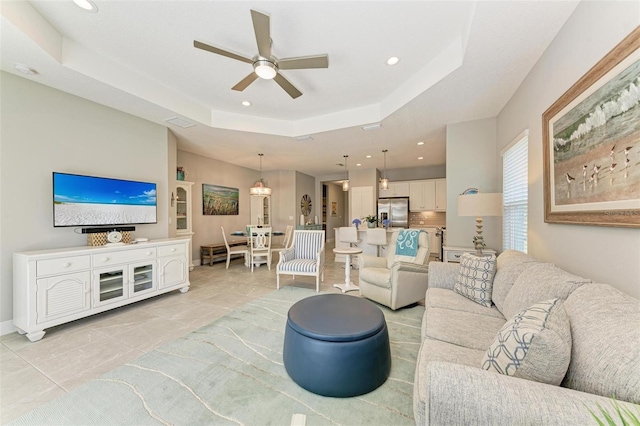 living room featuring light tile patterned flooring, ceiling fan, and a tray ceiling