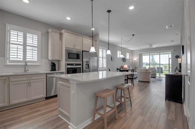 kitchen with sink, backsplash, light hardwood / wood-style floors, a kitchen island, and appliances with stainless steel finishes