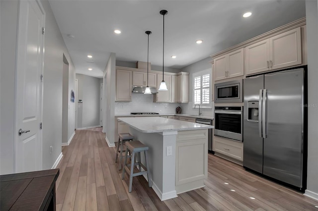 kitchen with appliances with stainless steel finishes, light wood-type flooring, sink, decorative light fixtures, and a kitchen island