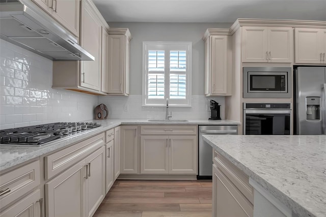 kitchen featuring light stone countertops, sink, stainless steel appliances, backsplash, and light hardwood / wood-style floors