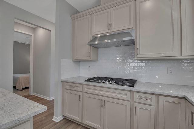 kitchen with backsplash, stainless steel gas stovetop, light stone countertops, and light wood-type flooring