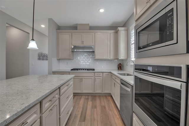 kitchen with appliances with stainless steel finishes, light stone counters, sink, decorative light fixtures, and light hardwood / wood-style flooring