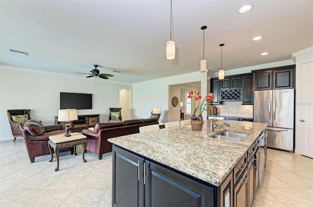 kitchen featuring ceiling fan, pendant lighting, sink, stainless steel refrigerator, and an island with sink