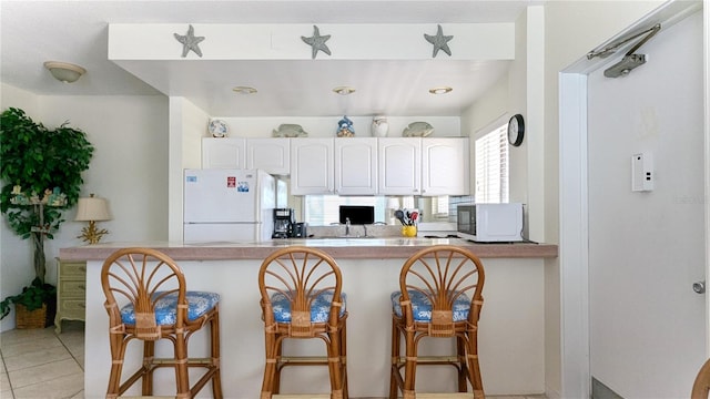 kitchen featuring kitchen peninsula, a breakfast bar, white cabinets, and white appliances