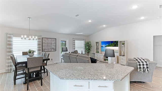 kitchen with hanging light fixtures, light hardwood / wood-style flooring, vaulted ceiling, a kitchen island, and white cabinetry