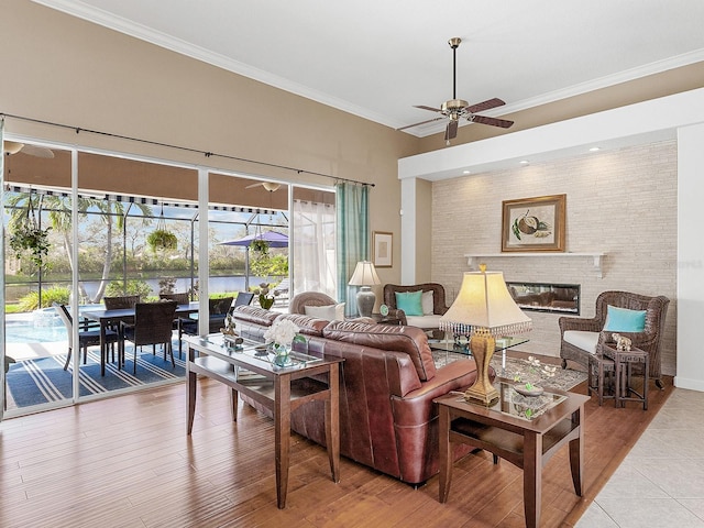 living room with a fireplace, light hardwood / wood-style flooring, ceiling fan, and crown molding