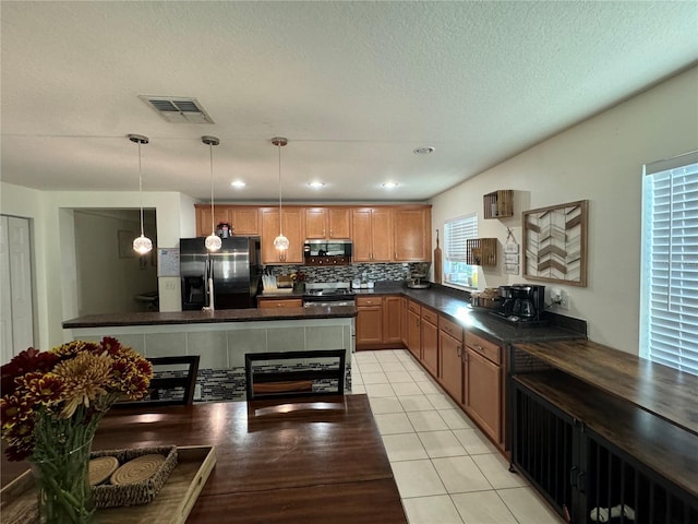 kitchen featuring hanging light fixtures, backsplash, a textured ceiling, light tile patterned floors, and appliances with stainless steel finishes