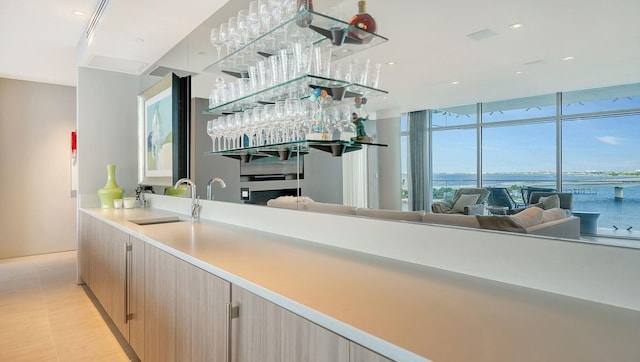 bar with light brown cabinetry, a water view, floor to ceiling windows, and sink