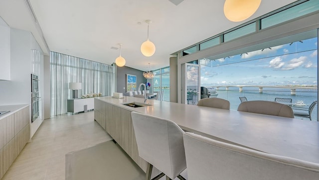 kitchen featuring stainless steel double oven, sink, pendant lighting, a water view, and a breakfast bar area