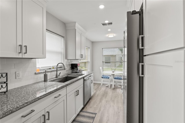 kitchen with white cabinetry, sink, stainless steel dishwasher, backsplash, and light wood-type flooring