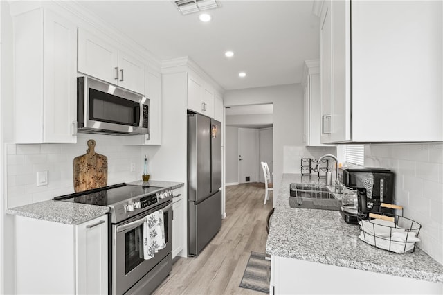 kitchen with light stone countertops, appliances with stainless steel finishes, sink, white cabinets, and light hardwood / wood-style floors