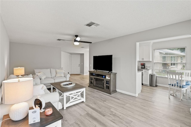 living room featuring a textured ceiling, light wood-type flooring, and ceiling fan