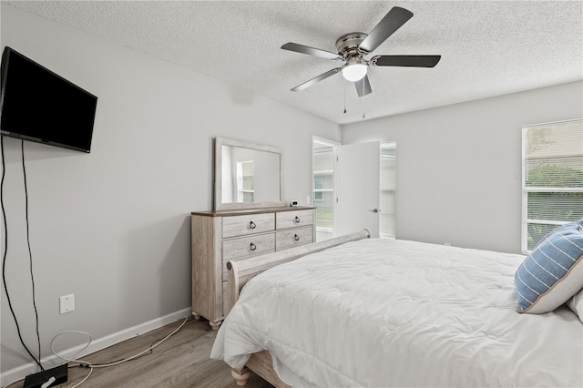 bedroom featuring multiple windows, ceiling fan, a textured ceiling, and light wood-type flooring