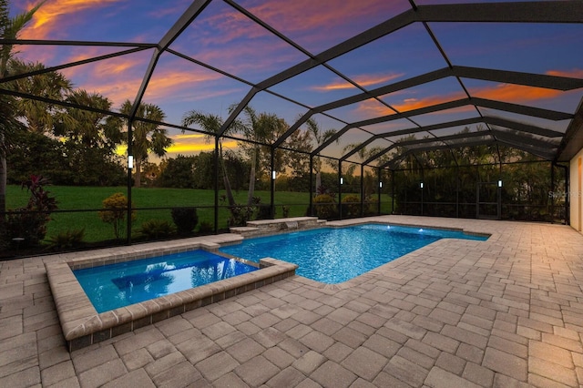 pool at dusk featuring glass enclosure, a patio area, and an in ground hot tub